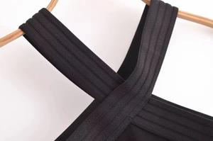 Détail des bretelles croisées d'une robe noire côtelée élastique sur cintre en bois