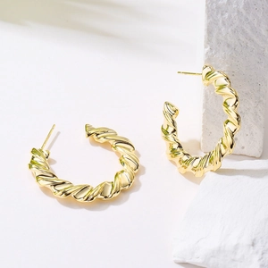 Textured gold-plated twist C-shape earrings displayed on a minimalist white stone pedestal