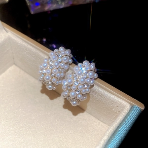 Close-up of luxury C-shaped earrings with white pearls and sparkling zircons in gold setting