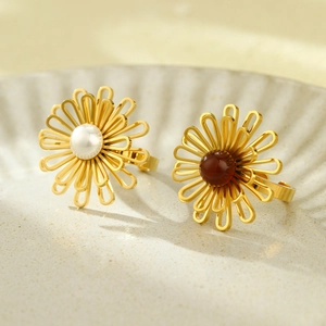 Golden flower rings with white pearl and red gemstone on a ceramic plate