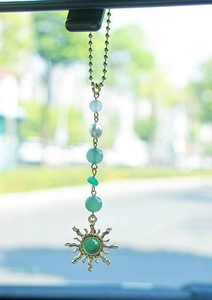 Detail of sun pendant car charm with green stone and pearls on rearview mirror