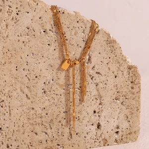Detail of 18K gold plated multi-layer chain with sequin tassels on light rock