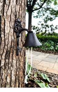 Detail of vintage cast iron garden bell with scrollwork bracket mounted on a tree trunk