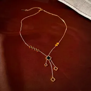 Collier en titane doré avec pendentif trèfle noir et pompons sur fond de soie