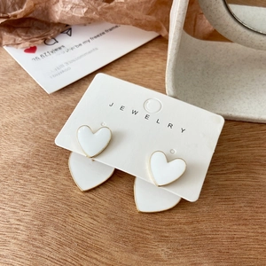 Detail of tiered heart earrings with white enamel and gold metal frame on display card