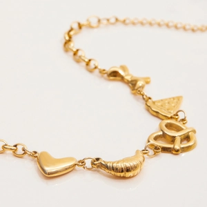 Close-up of 18K gold-plated charms including heart, croissant, and pizza on a bracelet