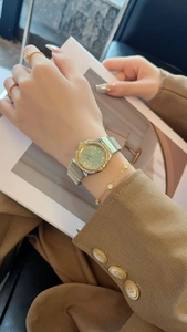 Detail view of a women's watch with green dial and rhinestones paired with gold jewelry