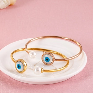 Detail of gold and rose gold evil eye bangles with pearls on a white ceramic plate