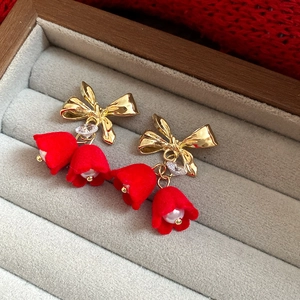 Macro detail of red velvet bell flower earrings with golden bows and pearls