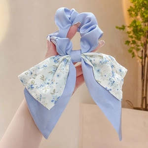 Detail of blue floral bow scrunchie with satin ribbon texture held in hand
