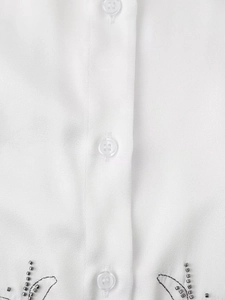 Detail of white blouse featuring translucent buttons and beaded embroidery with black lines