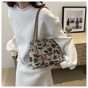 Detail of floral woven shoulder bag with elegant metal chain strap on female model