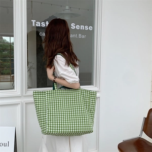 Detailed view of large green and white gingham tote bag worn by model in a minimal setting