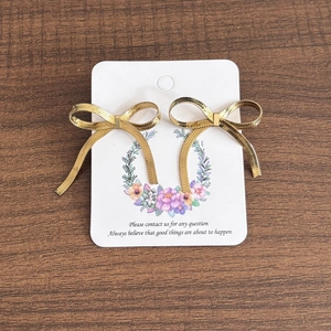 Detail of 18K gold stainless steel bow earrings with mesh texture on floral display card