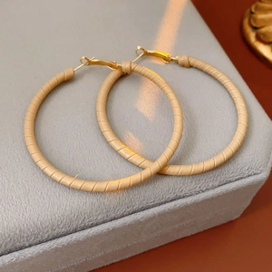 Macro shot of beige leather wrapped hoop earrings with gold metal on a velvet display