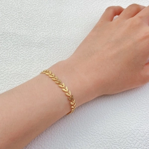 Detail of a gold leaf-shaped chain bracelet worn on a wrist against a white background