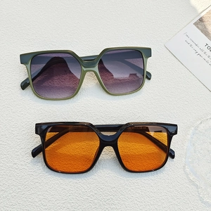 Square fashion sunglasses with olive green and black frames on a textured white background
