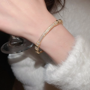 Close-up of gold-plated bangle with pavé zircons worn by a hand holding a crystal glass