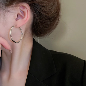 Close-up of polished silver large hoop earrings worn by a model in a black suit