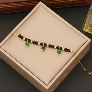 Detailed shot of golden stainless steel bracelet with green heart charms on jewelry box