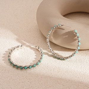 Detail of silver hoop earrings featuring turquoise bead inlay on a textured background