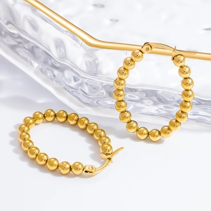 Detailed close-up of gold beaded hoop earrings on a decorative glass tray