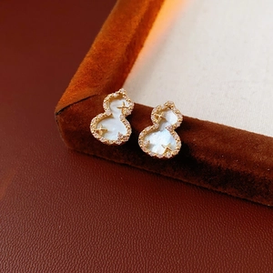 Macro shot of gold gourd earrings with white shell and inlay details on velvet