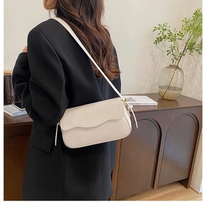 Close-up of a cream white PU leather shoulder bag with flap design and slim strap on model