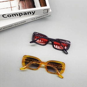Flat lay of oval sunglasses with purple and yellow frames on a minimalist book background