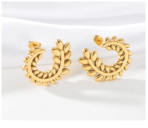 Macro shot of gold wheat ear C-shaped earrings on elegant white silk background