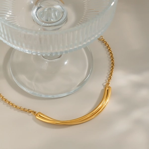 Detailed close-up of a minimalist gold curved cylinder pendant necklace on a beige backdrop