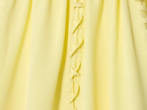 Detail van gele blouse met ronde hals en ingewikkeld geweven vetersluiting op de stof