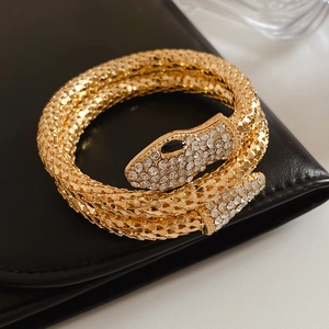 Close-up of golden snake wrap bracelet with crystal-pave head and textured metal finish