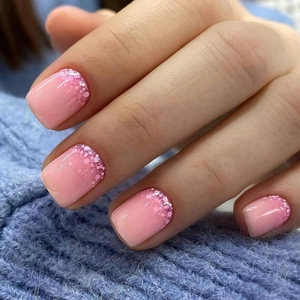 Faux ongles carrés courts avec dégradé rose pailleté portés sur une main