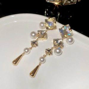 Macro detail of drop earrings with square crystals and pearls on white ceramic plate