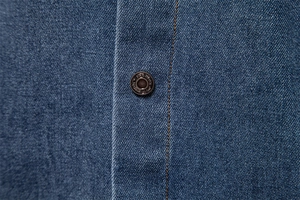 Detail of denim shirt buttons with orange stitching and twill texture on blue fabric