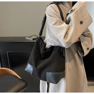 Detail of black suede tote bag featuring white contrast stitching and adjustable strap