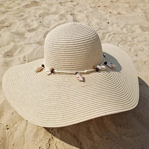 Detail of hand-woven straw hat texture with white shells and beads on sand beach