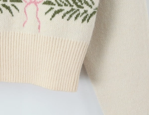 Close-up of white knit cardigan featuring green leaf jacquard and ribbed hem detail