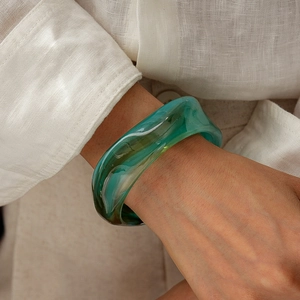 Close-up of translucent green acrylic bangle with wave design on model wearing white linen