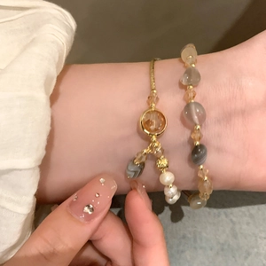 Detail of layered vintage faux pearl and amber crystal bracelets on a model's wrist
