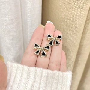 Detail shot of dainty black bow earrings with sparkling crystal accents and gold finish