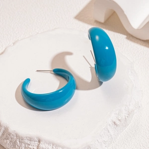 Macro shot of turquoise acrylic C-shaped earrings on a white minimalist stone base