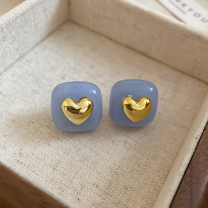 Close-up of blue square stud earrings with 3D golden heart in a jewelry box