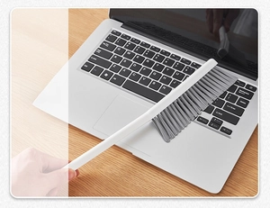 Detailed view of the long-handled cleaning brush removing dust from a laptop keyboard