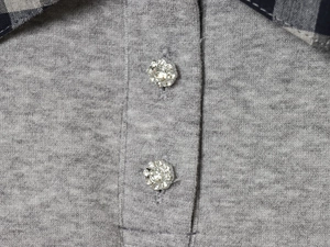 Detail of grey knit top with black and white plaid collar and flower rhinestone buttons