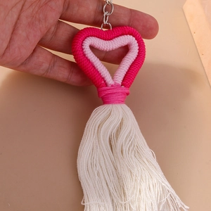 Close-up of hand holding a handmade woven heart keychain with pink tassels and metal ring
