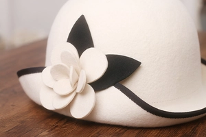 Detailed macro view of white wool felt hat featuring camellia flower and black edging