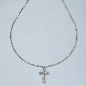 Macro shot of a silver vintage cross pendant with ornate textures and hip-hop style chain