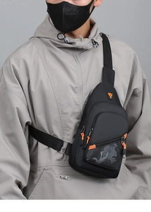 Detail of black chest bag featuring orange zipper pulls and subtle camo front pocket